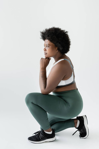 full length of curly african american plus size woman in sportswear sitting on white  - Foto, afbeelding