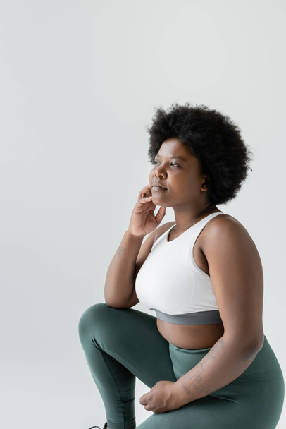thoughtful african american plus size woman in sportswear sitting on grey - Fotó, kép