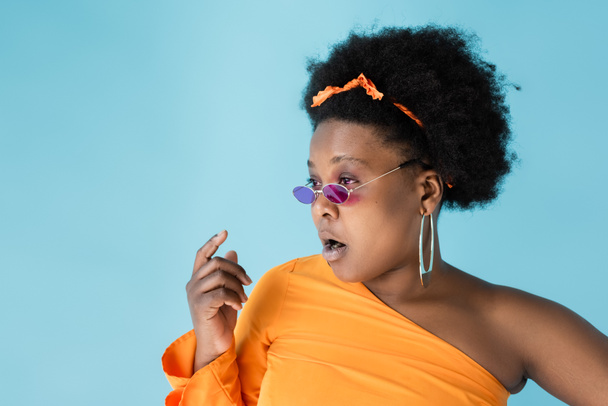 shocked african american body positive woman in pink sunglasses isolated on blue - Φωτογραφία, εικόνα