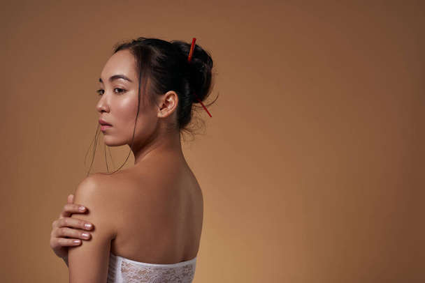 Side view of stylish asian girl hugging herself and looking away. Attractive young brunette woman wearing tank top. Female beauty. Isolated on orange background. Studio shoot. Copy space - Foto, afbeelding