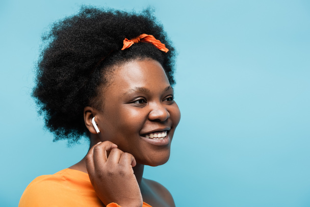 happy african american body positive woman in wireless earphone isolated on blue - Foto, imagen