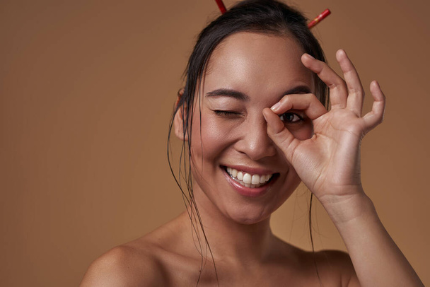 Partial of smiling elegant asian girl looking through binocular gesture. Beautiful young brunette slim woman. Female beauty. Isolated on orange background. Studio shoot. Copy space - Fotoğraf, Görsel
