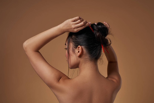 Partial back view of fashionable asian girl correcting her haircut. Pretty young brunette slim woman. Female beauty. Isolated on orange background. Studio shoot. Copy space - Fotografie, Obrázek