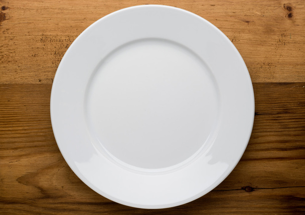 Empty white plate on wooden table - Фото, изображение