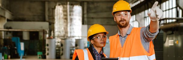 Multiracial man and woman in protective clothing working together at factory - 写真・画像