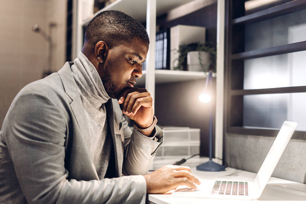 Genç siyahi Afrikalı adam masada otururken dizüstü bilgisayar teknolojisini kullanarak rahatlıyor. Genç yaratıcı Afrikalı adam evde klavyede çalışıyor ve daktilo kullanıyor. Ev konseptinde çalışıyor. - Fotoğraf, Görsel