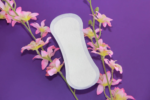 white women's daily sanitary pads and flowers on a purple background - Photo, Image