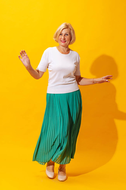 Studio shot of fashionable senior woman in summer style outfit isolated on bright yellow background. Concept of beauty, emotions, vacation, travel, ad and sales - Fotografie, Obrázek
