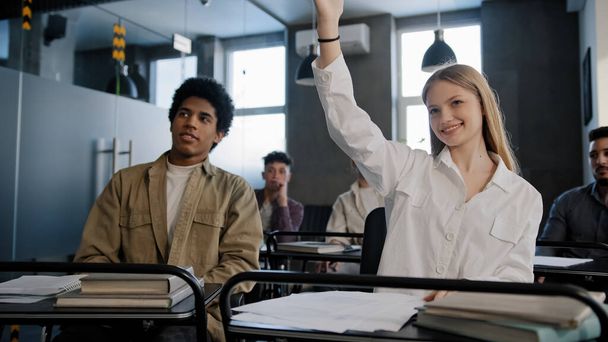 Diverse students classmates attentively listening to interesting lecture enthusiasm in classroom young caucasian girl raising hand knows answer answers question higher education concept in college - Photo, Image