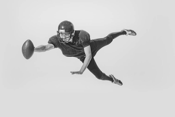 Dynamic portrait of young man, american football player catching ball. Black and white photography. Full equipment. Concept of sport, retro style, 20s, fashion, action, college sport, youth - Fotoğraf, Görsel