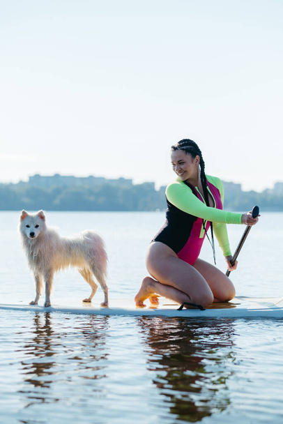 Щаслива жінка Paddleboarding на міському озері в ранньому ранку з її собакою Японська шпитсинка сидячи на Sup Board - Фото, зображення