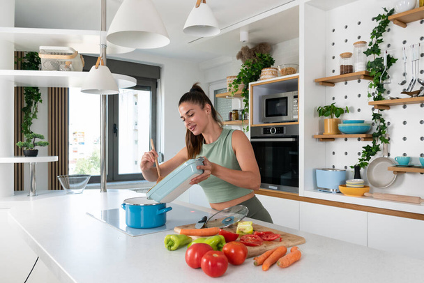 Young sporty woman cutting and cooking fresh natural vegetables at kitchen and cooking for healthy lunch. Self care yoga nutritionist girl having healthy meal after workout. - Foto, Bild