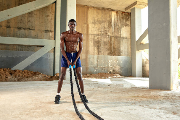 Rope workout. Sport man doing battle ropes exercise outdoor. Black male athlete exercising, doing functional fitness training with heavy rope. - Foto, Imagem