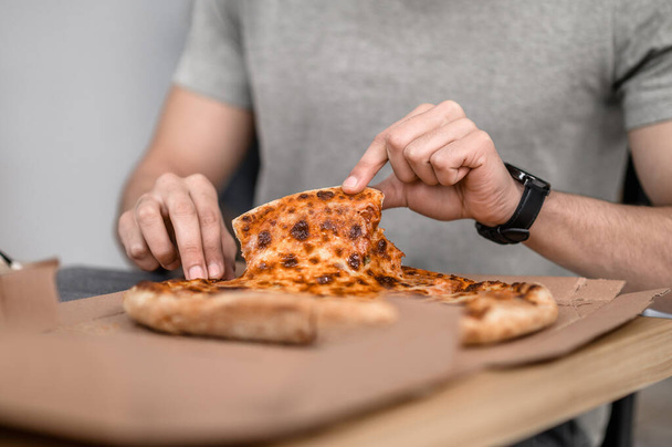 Piece of pizza. Mens neat hands taking piece of fresh appetizing pizza lying in box on table no face - Fotografie, Obrázek