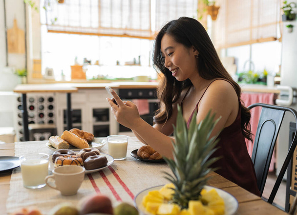 asian woman have breakfast at home while looking at her smartphone - Photo, Image
