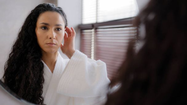 Worried upset young woman standing in bathroom in bathrobe reflected in mirror looking at split ends brittle damaged dry hair unhappy girl feeling frustration about unhealthy long curly fragile hair - Fotoğraf, Görsel