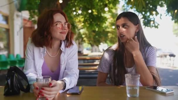 Menschen, Kommunikation und Freundschaftskonzept - lächelnde junge Frauen im Café im Freien - Filmmaterial, Video