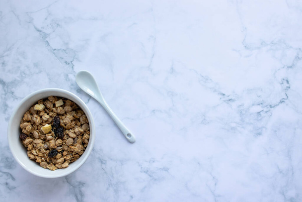 Bowl of homemade granola cereal with a ceramic spoon on white marble table background. Top view, flat lay, copy space. Healthy eating concept.  - Foto, imagen