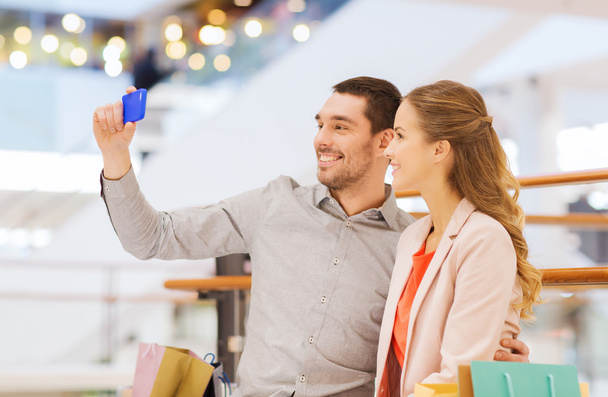 счастливая пара со смартфоном, делающая селфи в торговом центре
 - Фото, изображение