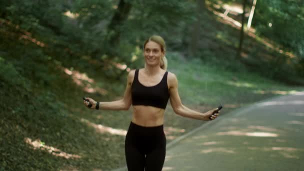 Тренировка сердца. Счастливая женщина средних лет спортсменка прыжки на скакалке, тренировки на открытом воздухе в лесу или общественном парке, замедленная съемка - Кадры, видео