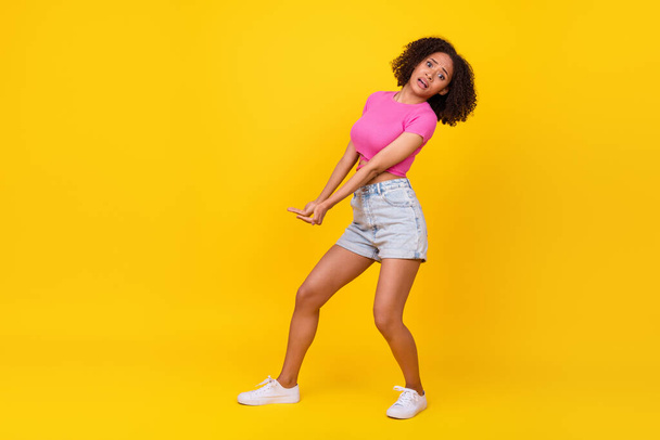 Full size profile portrait of amazed hardworking girl arms hold empty space isolated on yellow color background. - 写真・画像