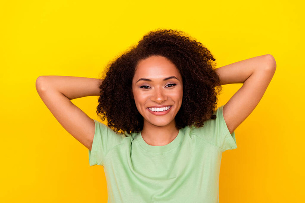 Photo of pretty charming lady wear green t-shirt arms behind head smiling isolated yellow color background. - Fotó, kép