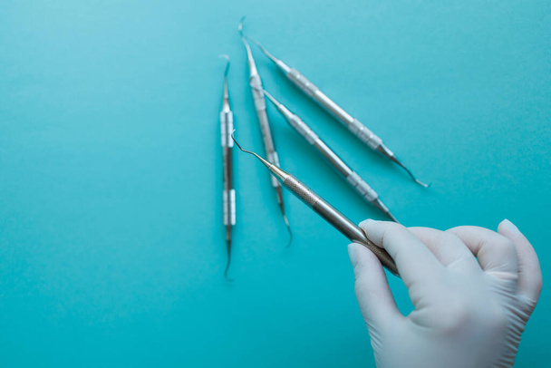Рука стоматолога в латексній рукавичці, що приймає зубні інструменти на синьому фоні
 - Фото, зображення
