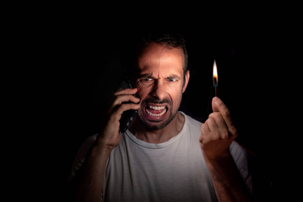 Angry man talking on the phone with a match in the dark. Blackout concept. Selective focus. - Photo, image