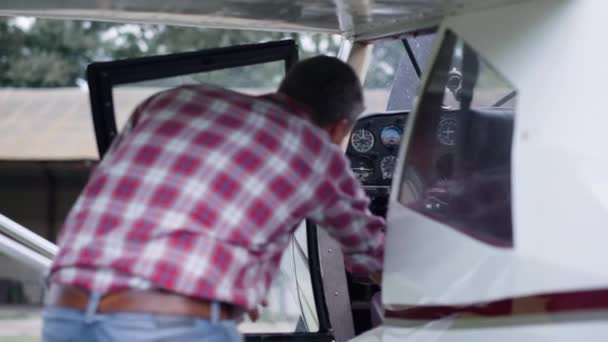 Professional pilot taking seat cabin white private airplane on aerodrome. Man aviator entering in ultralight aircraft before sky flight. Aviation engineer sitting cockpit to drive air transport. - Filmagem, Vídeo