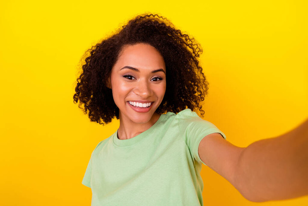 Photo of adorable pretty girl dressed green t-shirt smiling tacking selfie isolated yellow color background. - Foto, afbeelding