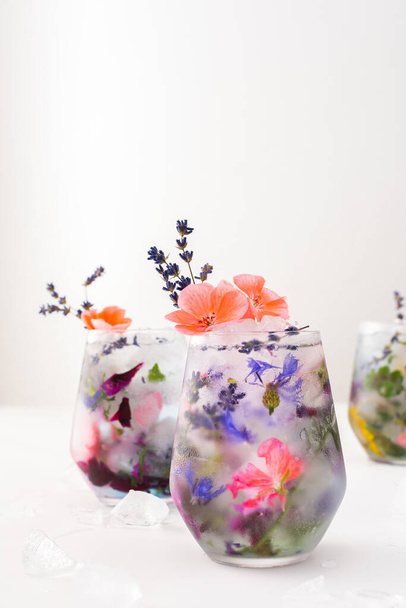 Refreshing cold drink with frozen flowers, cornflowers and geraniums, osteosperum and lavender and carnation - Foto, Imagen