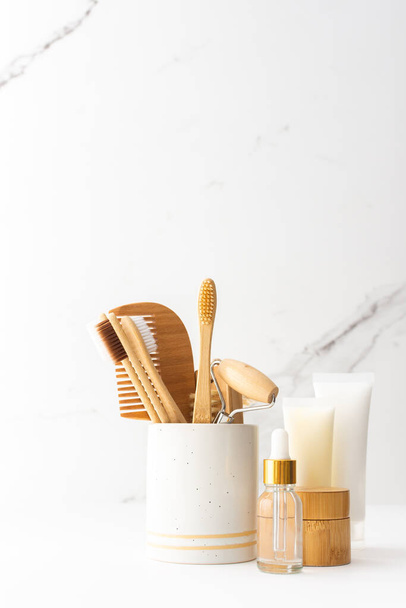 Wooden toothbrushes with natural bristles in a ceramic glass, face and skin care products, bottles with a pipette and a jar of cream, bath accessories, spa and beauty concept - Foto, imagen