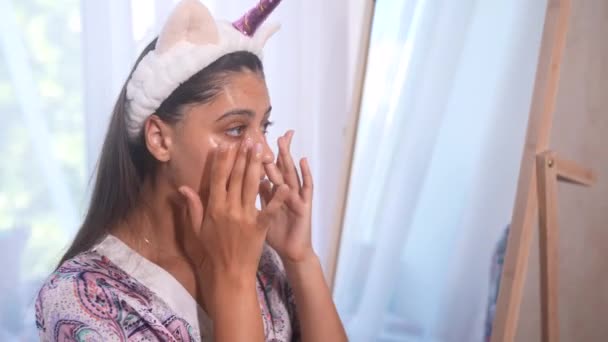 Mladá modelka aplikující kosmetické ošetření krému na obličej - Záběry, video