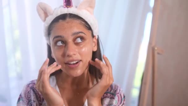 Jeune modèle appliquant un traitement cosmétique à la crème sur son visage - Séquence, vidéo