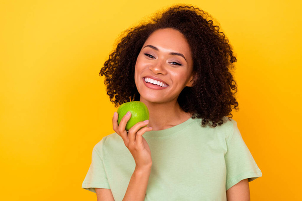 Photo of cheerful positive lady wear green t-shirt eating apple white teeth empty space isolated yellow color background. - Фото, зображення