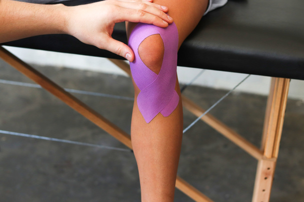 Physiotherapist applying kinesiology tape to patient knee. Therapist treating young female athlete. Kinesiology taping. Post traumatic rehabilitation,sport physical therapy. - Foto, immagini