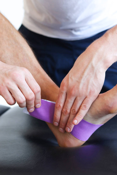 Kinesiology taping treatment with purple tape on male patient injured foot. Sports injury kinesio treatment. - 写真・画像
