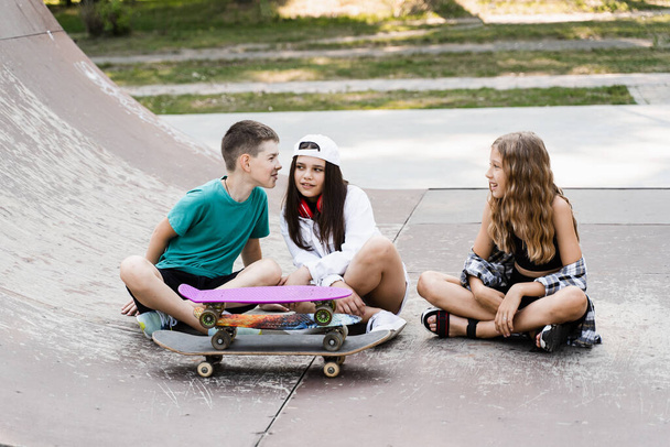 Дети со скейтбордом и досками общаются и обсуждают на спортивной площадке. Концепция детской дружбы. Дети улыбаются, смеются и веселятся вместе - Фото, изображение