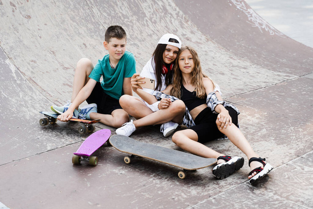 Children with skateboard and penny boards making selfie on phone on the sports playground. Children friendship concept. Kids smile and laugh and have fun together - Foto, Bild
