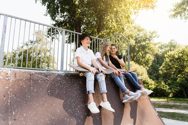 Kids smile and laugh and have fun together. Children with skateboard and penny boards communicate and discuss on the sports playground. Boy and girls friendship concept - Foto, imagen