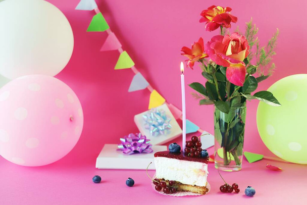 Десерт с белым кремом украшен свежими ягодами и горящей свечой, свежими розами, воздушными шарами и подарками на столе, с днем рождения, праздником, поздравлениями, открыткой - Фото, изображение