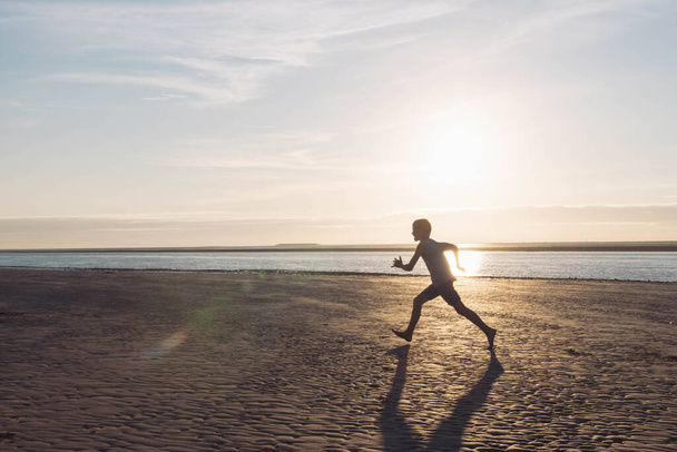 a boy runs on the beach at sunset, a silhouette of a child running on the beach on the sand near the water, there is a place for an inscription. High quality photo - Photo, image