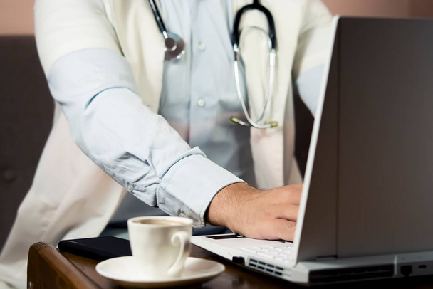 Mieslääkäri käyttää kannettavaa tietokonetta, jossa on valkoinen mockup-näytön tekniikka etälääketiede e verkkosivuilla mainos, katselu e-oppimisen lääketieteellinen online-etäterveydenhuolto webinar, kirjoittaa raportti. Olkapään yli - Valokuva, kuva