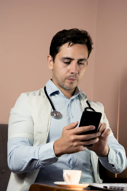 Крупный план врача по телефону в его офисе, врач, работающий онлайн, онлайн консультация. Неузнаваемый врач пользуется смартфоном на рабочем месте, беседует с пациентом, назначает лечение - Фото, изображение