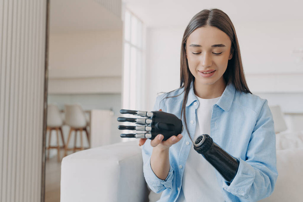Disabled young woman is assembling bionic arm with hand. Prosthesis is connecting in wrist joint. Cyber sensor hand has processor chip and buttons. European girl has high tech carbon electronic hand. - Foto, Imagen