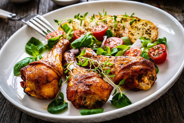 Barbecue chicken drumsticks with fried potato, lettuce and mini tomatoes on wooden table  - Photo, image