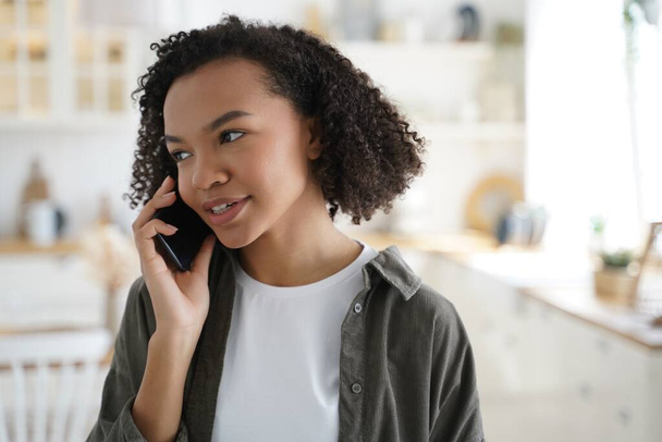 Modern african american girl talking on smartphone at home, stylish young woman with afro hairs answer mobile phone call, having conversation with friends or relatives indoors. - Fotoğraf, Görsel