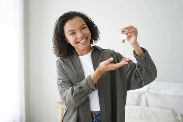 Happy biracial female buyer tenant of new home flat showing house keys. Young mixed race woman homeowner looking at camera demonstrates key of modern apartment. Mortgage, rental properties. - Fotó, kép