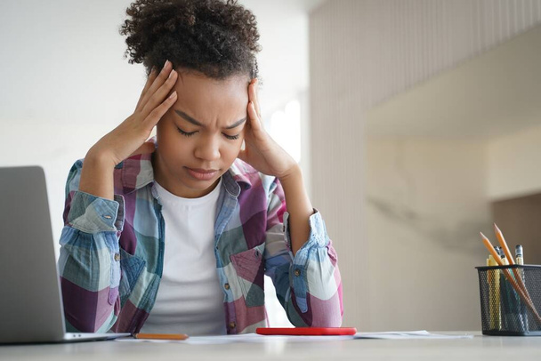 Tired african american teenage schoolgirl suffer headache while doing homework at laptop at home. Exhausted, frustrated teenager girl worried about educational problem or bullying. Difficult elearning - Zdjęcie, obraz