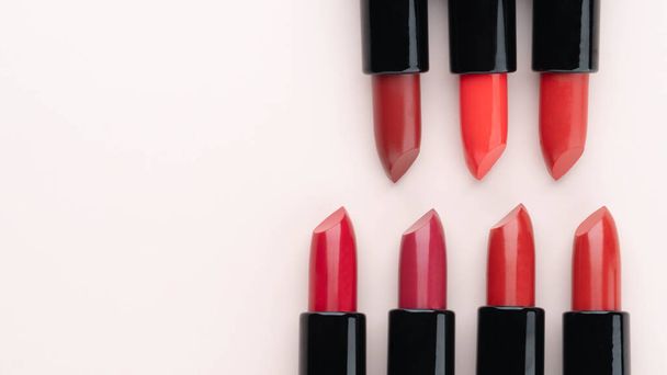Red lipsticks of different shades arranged in a circle on beige background. Makeup and cosmetics concept. Close up. Flat layout. Copy space. - Φωτογραφία, εικόνα